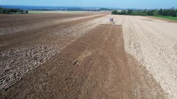 De trekker ploegt de grond met eggen. Uitzicht vanaf de drone. De landbouwmachines zijn uitgerust met GPS. — Stockvideo