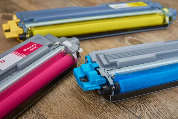Tahta masaya yerleştirilmiş renkli lazer yazıcı için üç toner fişeği.