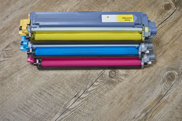 Yellow, cyan and magenta toner cartridges stacked horizontally on wooden table