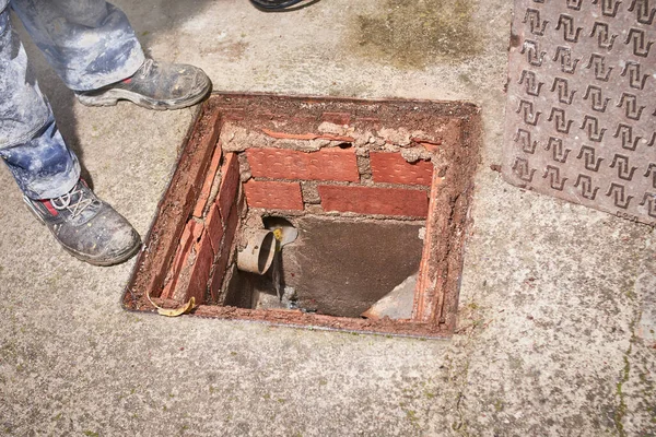Tesisatçı, tıkanıklığı açmak için sıkışan bir evin kanalizasyon kapağını açtı.