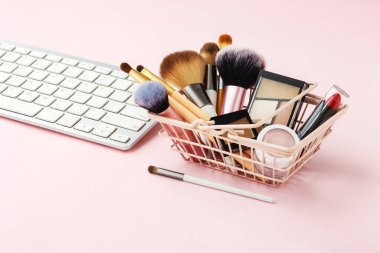 Makyaj ve kozmetik online alışveriş, alışveriş sepeti ve bilgisayar klavyesi ve pastel pembe masa üzerinde ürünler.