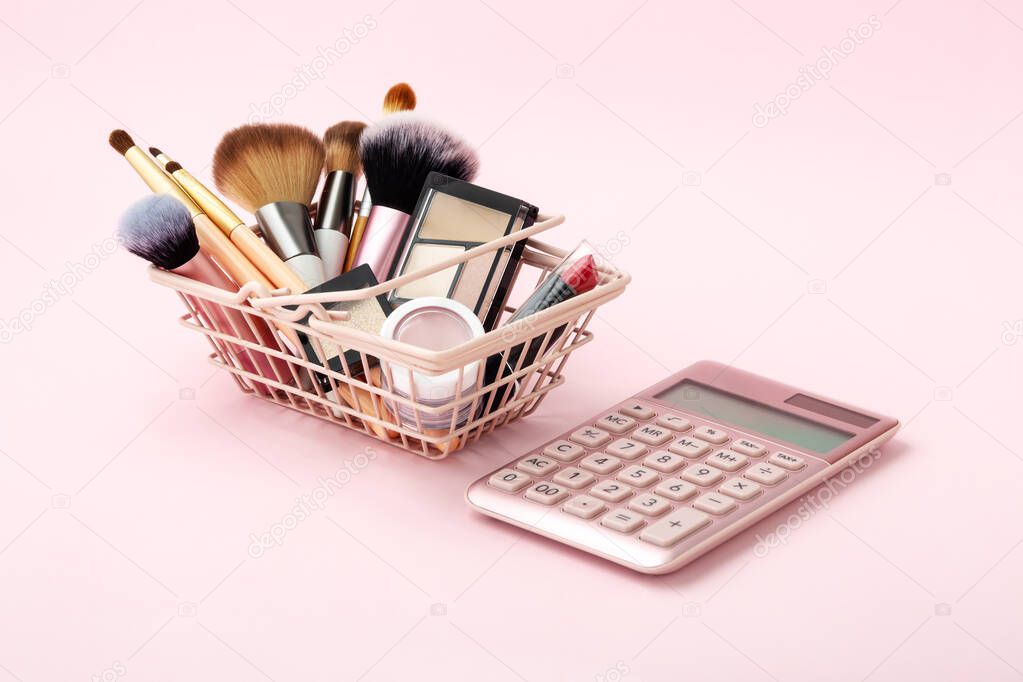 Makeup beauty products in shopping basket with calculator on pastel pink background