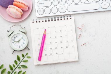 Pembe kalemli takvim, badem kurabiyesi ve mermer masadaki saat, kopyalama alanı olan üst görünüm