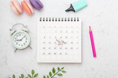 İğneli takvim, pembe kalem, badem kurabiyesi ve mermer zemin üzerindeki saat, üst görünüm