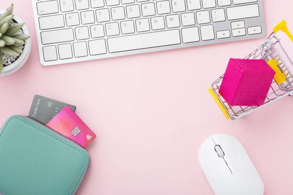 Shopping online concept with computer keyboard, credit card and shopping cart on pink background, top view with copy space