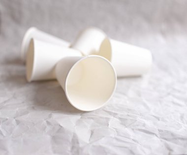 Beyaz kağıttan yapılmış tek kullanımlık bardaklar, geometrik desenli gri buruşmuş kağıtların üzerine serilmiştir.