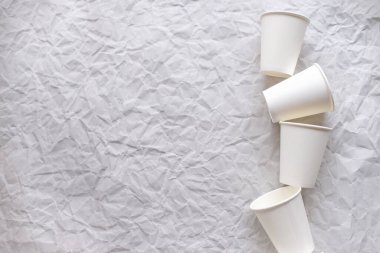 Beyaz kağıttan yapılmış tek kullanımlık bardaklar, geometrik desenli gri buruşmuş kağıtların üzerine serilmiştir.