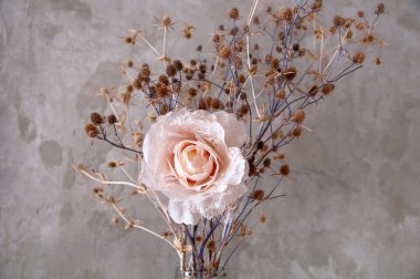 Beton bir duvarın arka planında suni bir gülle kurumuş yabani çiçekler.