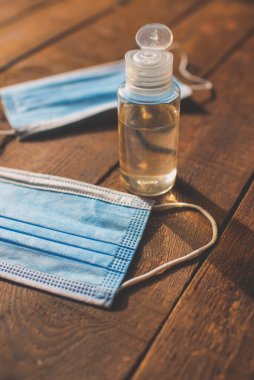 Üzerinde el dezenfektanı ve tek kullanımlık maskeler olan plastik şişe ahşap bir masada yatıyor.