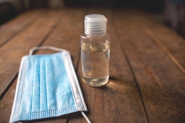 Üzerinde el dezenfektanı ve tek kullanımlık maskeler olan plastik şişe ahşap bir masada yatıyor.