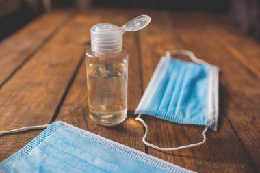 Üzerinde el dezenfektanı ve tek kullanımlık maskeler olan plastik şişe ahşap bir masada yatıyor.
