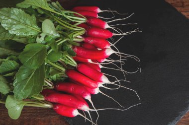 Kökleri ve yaprakları olan taze turp siyah granit kaide tahtasının üzerinde yatıyor.