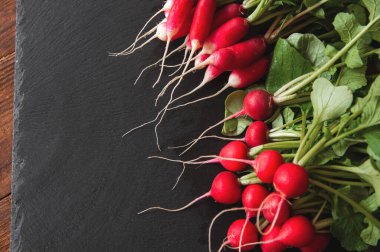 Kökleri ve yaprakları olan taze turp siyah granit kaide tahtasının üzerinde yatıyor.