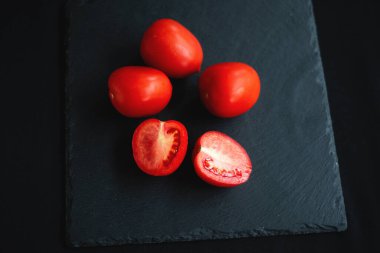 Bir grup domates, ikiye bölünmüş, servis için siyah bir tahtada duruyor.