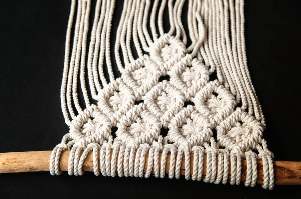 Close-up of hand made macrame texture pattern. Handmade macrame 100 cotton wall decoration with wooden stick. Modern decoration in the interior.