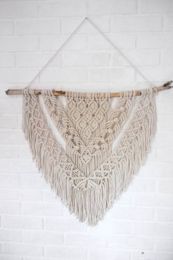 Beyaz bir duvara asılı ahşap çubukla el yapımı 100 adet pamuk duvar süslemesi. DIY boho ev dekorasyonu, çevre dostu modern örgü. İç mekanda modern dekorasyon.