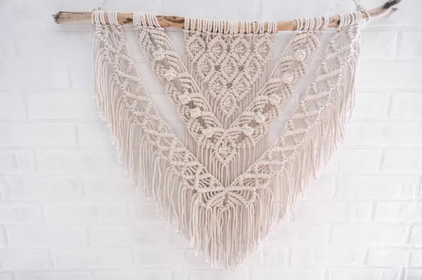 Handmade macrame 100 cotton wall decoration with wooden stick hanging on a white wall. DIY boho home interior decor, eco friendly modern knitting. Modern decoration in the interior.