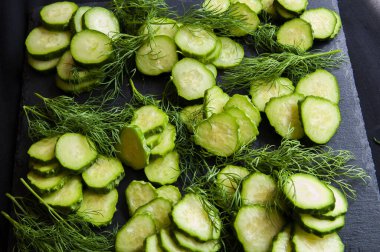 Siyah arka plandaki ev bahçesinden taze salatalıklar, taştan yapılmış sahte bir tahta. Salatalıklar parçalara ayrılır ve dereotu deseninde sıralanır..