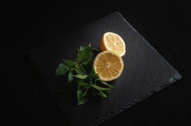 Ingredients for mojito summer citrus cocktail with lemon and mint. Peppermint with citrus on a black board for serving