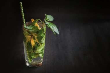 Mojito summer citrus cocktail with lemon and mint. Glass with peppermint with citrus on a black background