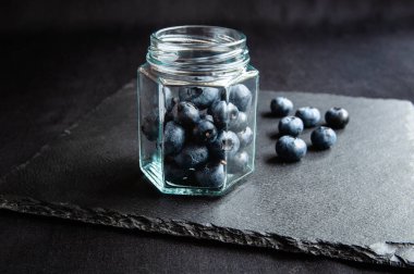 Cam bir kavanozda taze yabanmersini ve siyah bir tahtanın üzerine serilmiş. Sağlıklı beslenme ve vejetaryenler için yabanmersini.