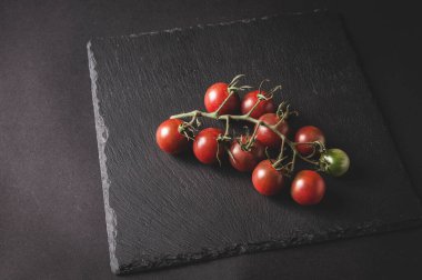 Bir daldaki taze vişneli domatesler siyah servis tahtasının üzerinde yer alır.