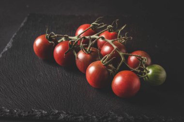 Bir daldaki taze vişneli domatesler siyah servis tahtasının üzerinde yer alır.