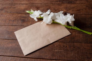 Tahta bir masanın üzerinde beyaz gladioli buketi ve eski tarz bir zarf.