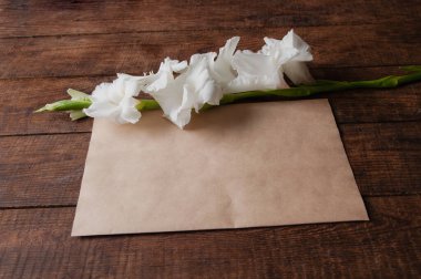 Tahta bir masanın üzerinde beyaz gladioli buketi ve eski tarz bir zarf.