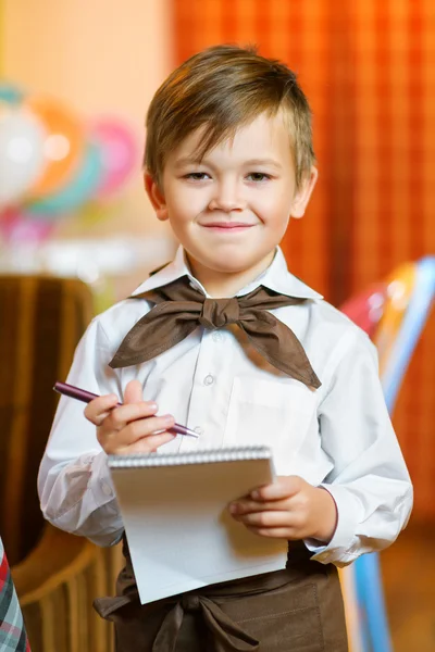 Happy cute boy waiter in apron writing order and looking at camera