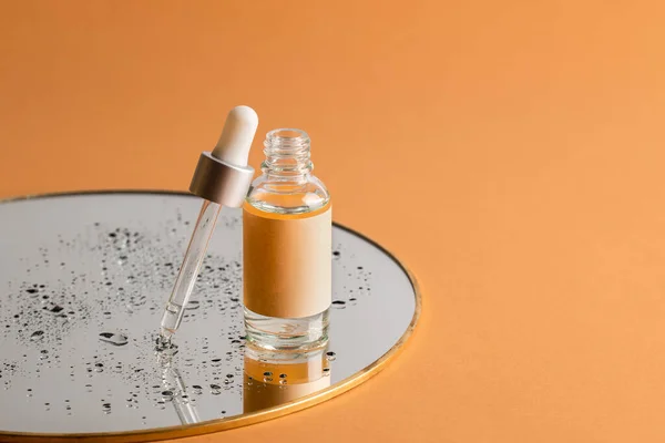 Açık turuncu arka planda damlaları olan bir aynada deri bakımı için pipeti olan şeffaf bir serum şişesi. Sağlık ve güzellik kavramı.