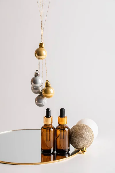 Noel minimalist kompozisyonu. Aynada iki kahverengi cam serum şişesi ve altın toplar asılı. Sağlık ve güzellik konsepti. Boşluğu kopyala