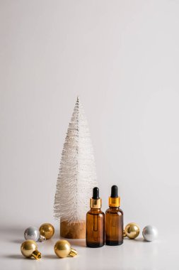 Noel ağacının arka planında iki kahverengi cam serum şişesi ve altın toplar olan minimalist bir Noel kompozisyonu. Sağlık ve güzellik konsepti. Boşluğu kopyala