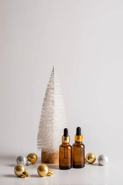 Noel ağacının arka planında iki kahverengi cam serum şişesi ve altın toplar olan minimalist bir Noel kompozisyonu. Sağlık ve güzellik konsepti. Boşluğu kopyala — Stok fotoğraf