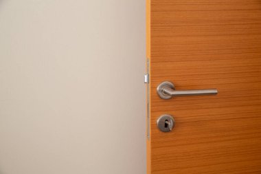 Beyaz duvarın önünde duran ahşap kapı. Kapı kilidi ve anahtar