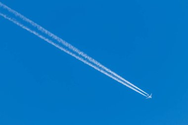 Mavi gökyüzünde uzun, beyaz, dumanlı egzoz dumanı ve jet yıkamasıyla uçan uçak, pilotlarla uluslararası ulaşım ve küreselleşme tatillerini gösteriyor.