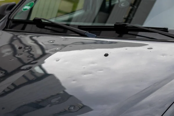 Car engine hood with many hail damage dents show the forces of nature and the importance of car insurance and a replacement value insurance against hail storm and storm hazards or extreme weather