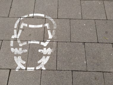 Asfalttaki yüz maskesi tabelasında COVID hastalığını önlemek için yüz maskesi takan bir kişinin resimli resmi görülüyor. Salgın zamanlarında ve ikinci dalga dalgalarında şehir merkezinde yüz kaplaması için 19 enfeksiyon.