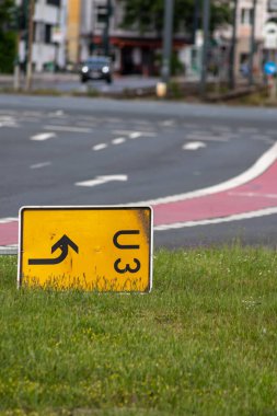 Yellow traffic sign for redirection on urban streets forces navigation system to calculate a new route for correct routing to reach your destination on German roads lying on grass after heavy storm
