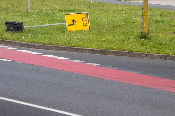 Yellow traffic sign for redirection on urban streets forces navigation system to calculate a new route for correct routing to reach your destination on German roads lying on grass after heavy storm