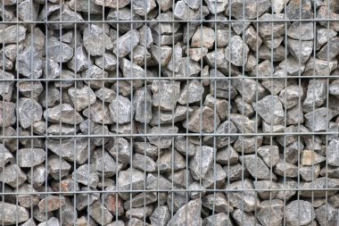 Protective gabions with grey broken stones behind grid as solid fence and solid wall and decorative element in gardens with rough surface textured as rock background and natural modern architecture