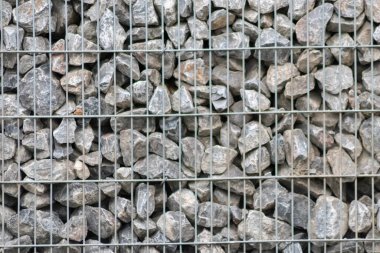 Protective gabions with grey broken stones behind grid as solid fence and solid wall and decorative element in gardens with rough surface textured as rock background and natural modern architecture