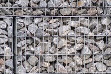 Protective gabions with grey broken stones behind grid as solid fence and solid wall and decorative element in gardens with rough surface textured as rock background and natural modern architecture