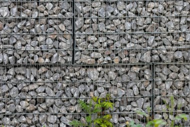 Protective gabions with grey broken stones behind grid as solid fence and solid wall and decorative element in gardens with rough surface textured as rock background and natural modern architecture