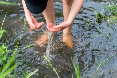 Küçük bir derede çıplak ayakla temiz suyla oynayan genç bir çocuk ayaklarını ve su kaynağını kullanarak ayak parmaklarını ve bacaklarını serinletiyor ve zen meditasyon atmosferindeki saf yaşam iksiriyle ferahlatıyor.