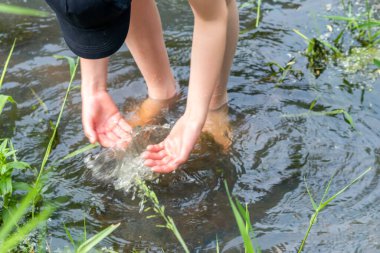 Küçük bir derede çıplak ayakla temiz suyla oynayan genç bir çocuk ayaklarını ve su kaynağını kullanarak ayak parmaklarını ve bacaklarını serinletiyor ve zen meditasyon atmosferindeki saf yaşam iksiriyle ferahlatıyor.