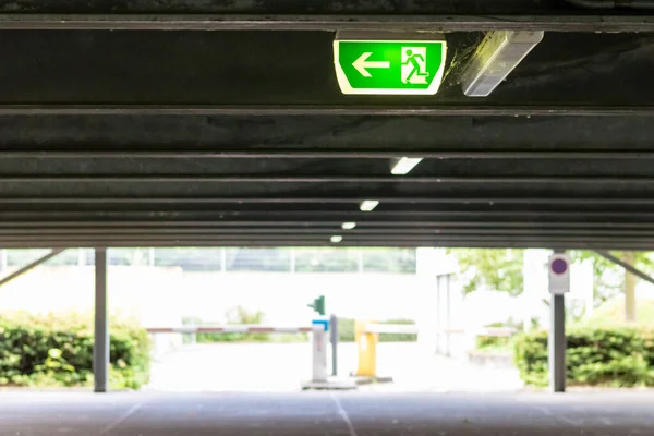 Green exit sign with running person and green arrow shows guidance system signage in a parking lot for rescue and evacuation safety in dangerous situations at ceiling rescues life in extreme danger