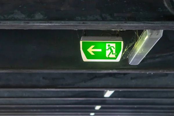 Green exit sign with running person and green arrow shows guidance system signage in a parking lot for rescue and evacuation safety in dangerous situations at ceiling rescues life in extreme danger