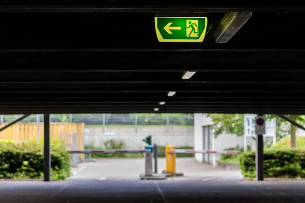 Green exit sign with running person and green arrow shows guidance system signage in a parking lot for rescue and evacuation safety in dangerous situations at ceiling rescues life in extreme danger