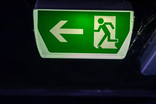 Green exit sign with running person and green arrow shows guidance system signage in a parking lot for rescue and evacuation safety in dangerous situations at ceiling rescues life in extreme danger